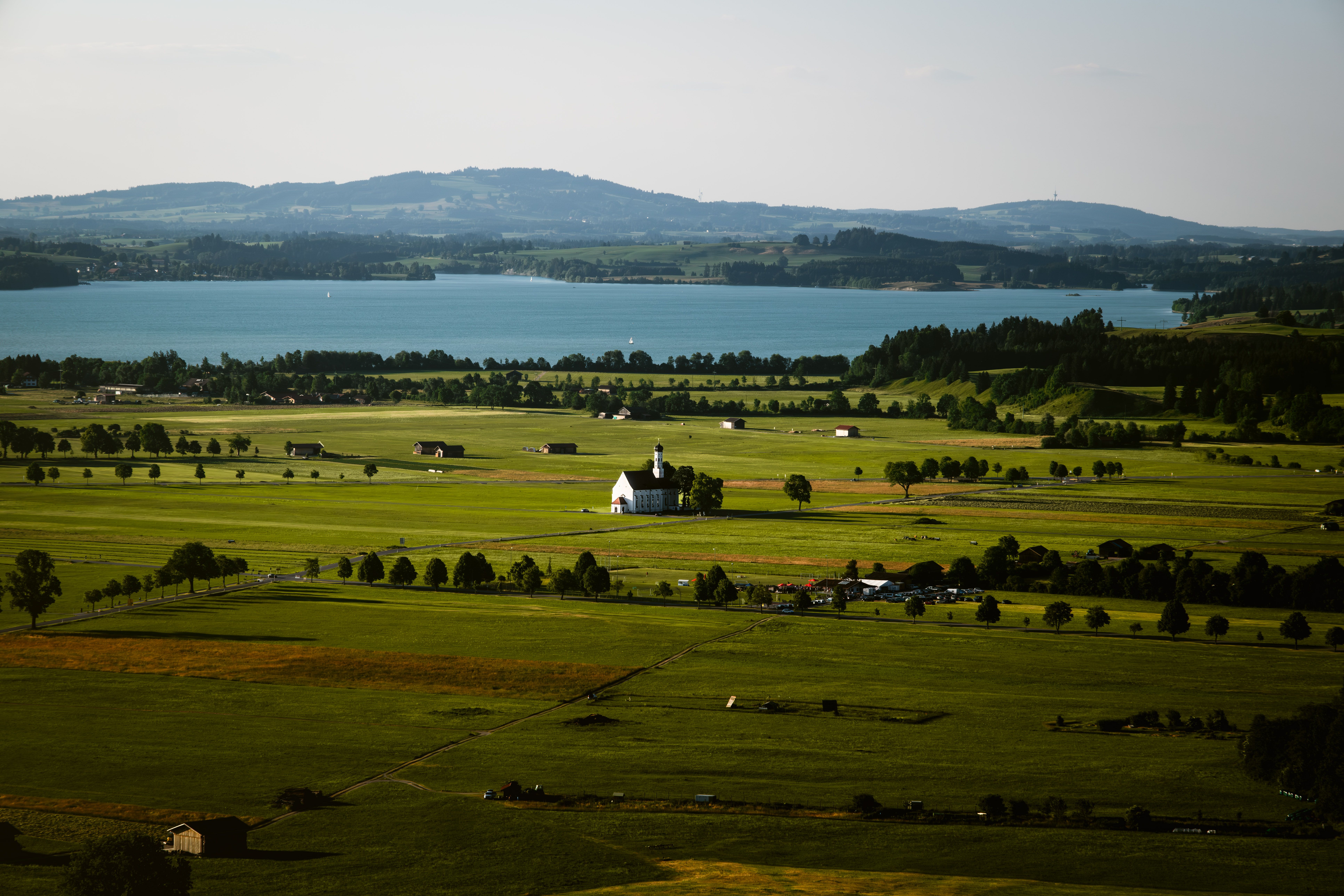 Aerial view of Füssen, Bavaria, with a village church, green fields, and a peaceful alpine lake.