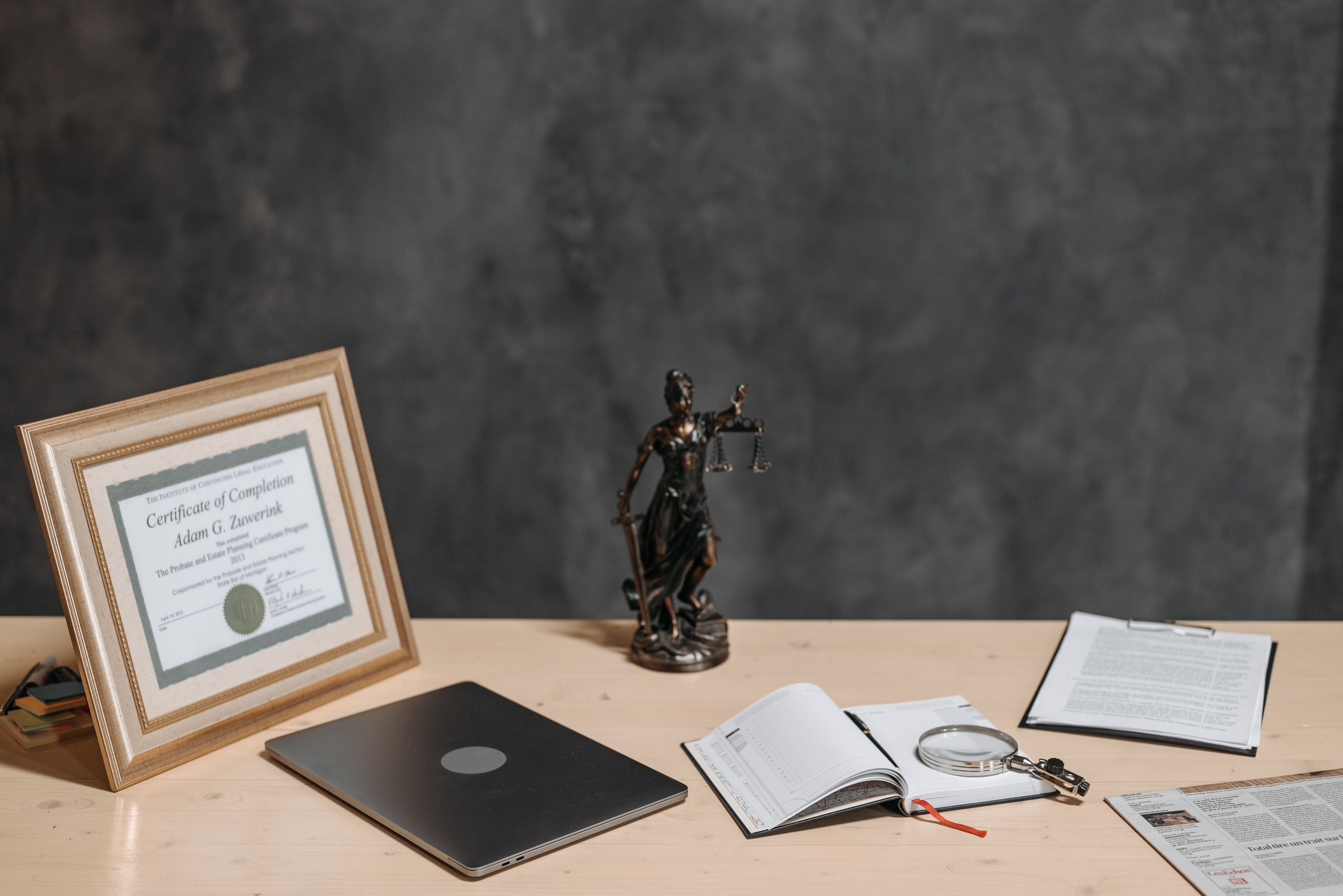 A lawyer's desk with a justice statue, laptop, magnifying glass, and legal documents